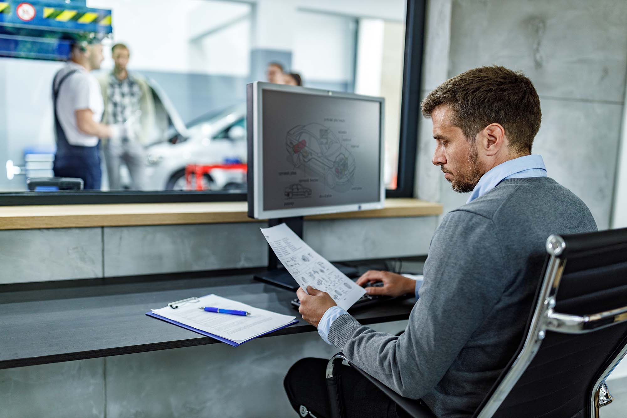 En man sitter framför en dator i en bilverkstad